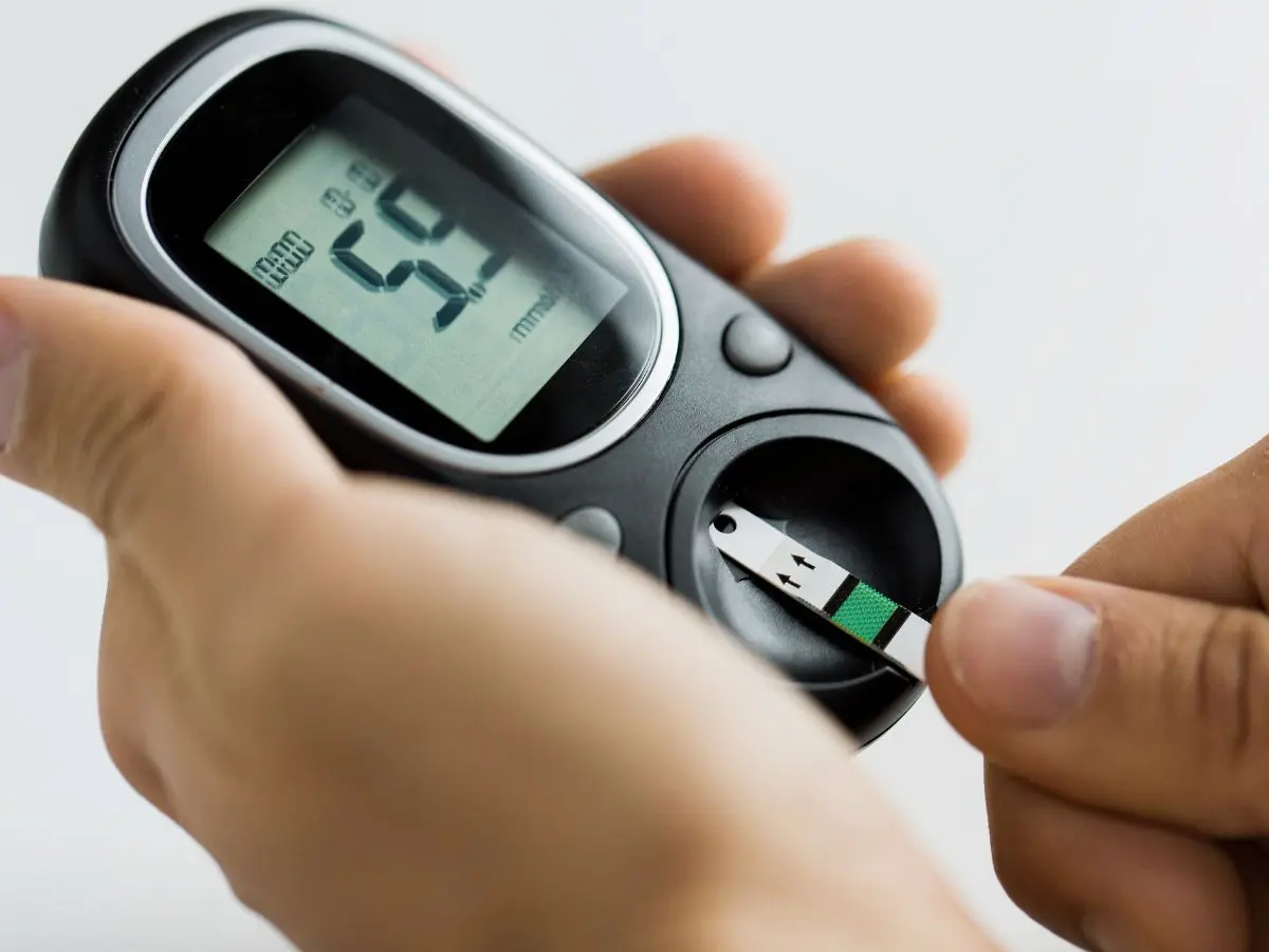 Checking blood sugar: Hands inserting a test strip into a digital glucometer device.